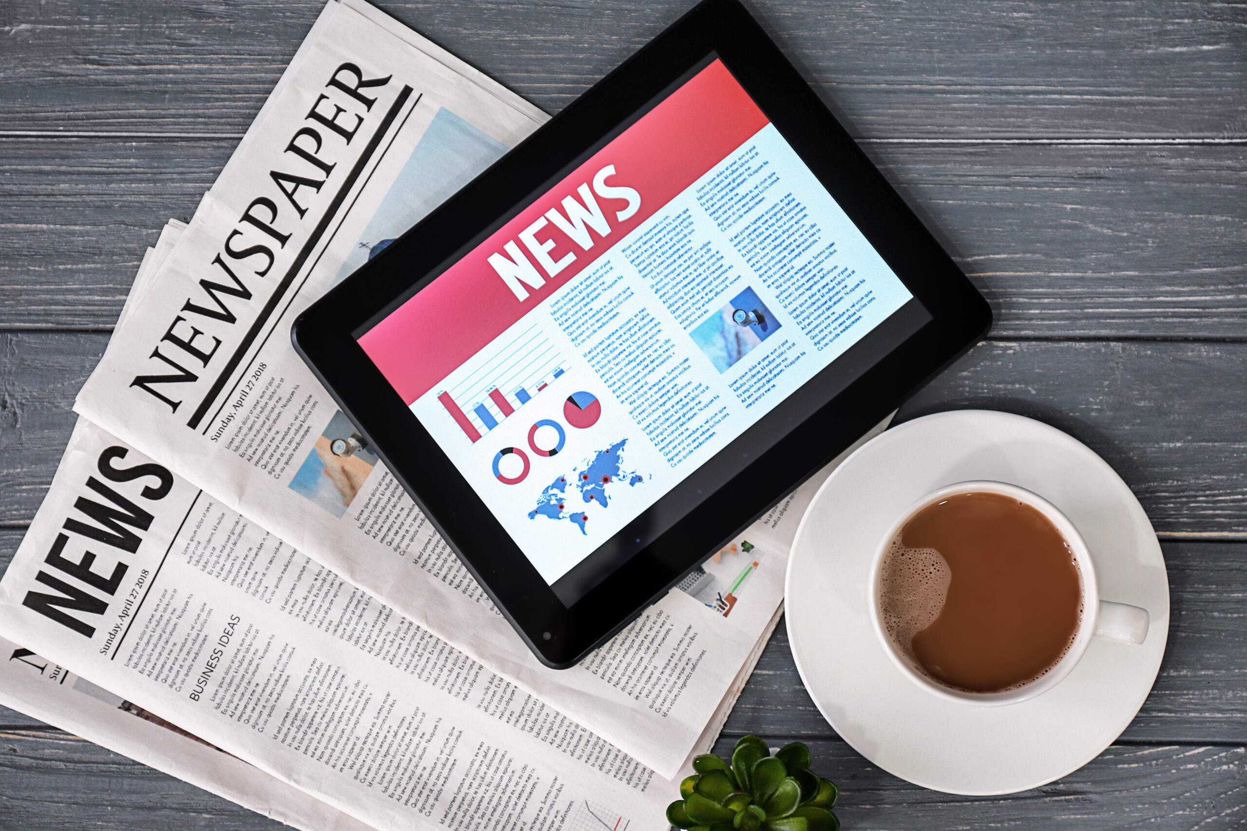 Tablet computer with news on screen and newspapers on wooden background